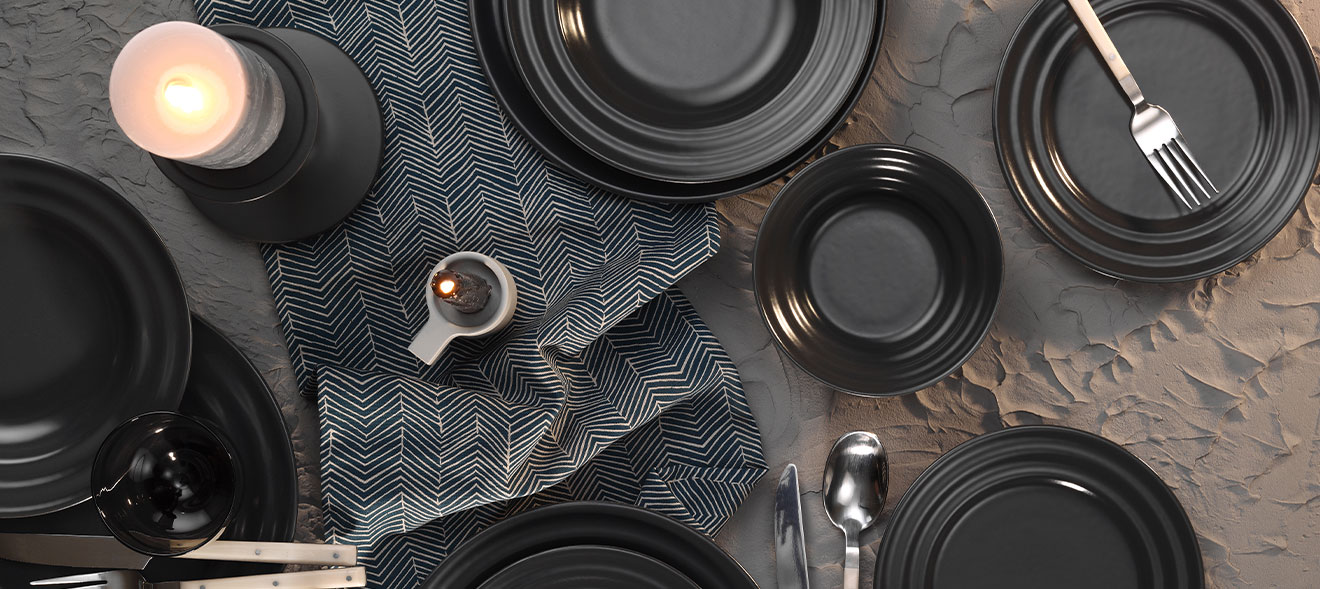 Schwarzes Geschirr von Kütahya auf einem Sandfarbenen, texturierten Hintergrund.